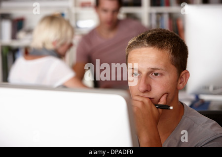 Junger Mann mit Computer, Hand am Kinn Stockfoto