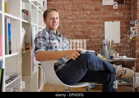 Porträt des jungen Mann sitzend auf Stuhl mit digital-Tablette Stockfoto