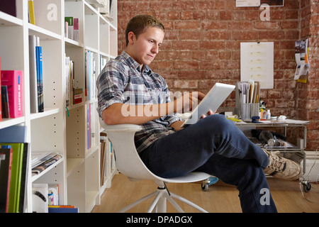 Junger Mann sitzend auf Stuhl mit digital-Tablette Stockfoto