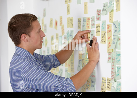 Junger Mann klebt Klebstoff Hinweis auf Wand Stockfoto