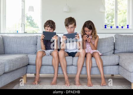 Brüder und Schwester auf Sofa mit digitalen Tablets und mobile Stockfoto