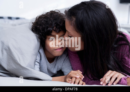 Mutter küssen Sohn auf Wange im Bett Stockfoto