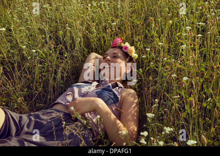 Junge Frau liegend auf Wiese mit Blumen im Haar Stockfoto