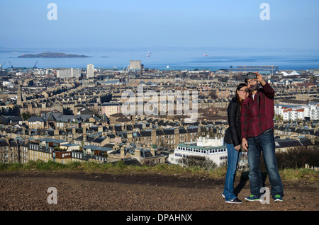 Eine junge asiatische paar nehmen ein Selbstporträt auf Calton Hügel mit North Edinburgh, Leith und den Firth of Forth im Hintergrund. Stockfoto