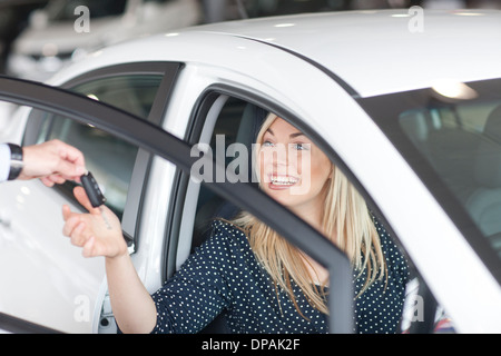 Junge Frau sitzt im neuen Auto mit Schlüssel im showroom Stockfoto