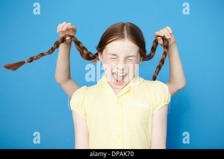 Mädchen Kleid gelb Schule, junge hinter ziehen ihre Zöpfe Stockfoto