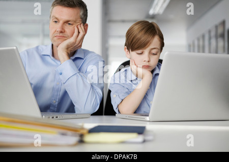 Vater und Sohn mit Notebooks schauen gelangweilt Stockfoto