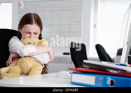 Mädchen sitzen im Büro umarmt Teddybär und Weinen Stockfoto