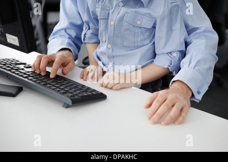 Junge sitzt auf Vaters Schoß mit Computer-Tastatur Stockfoto