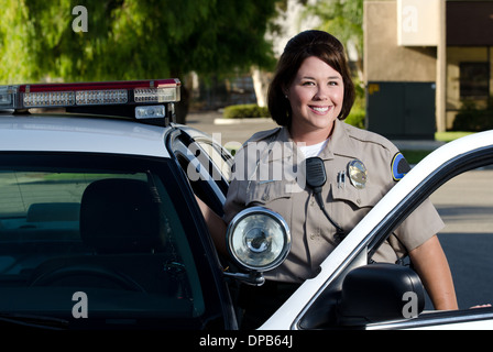 ein freundlich aussehende Polizist lächelt und steht neben ihrem Streifenwagen. Stockfoto
