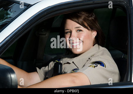 eine freundliche aussehende Polizistin sitzt und lächelt in ihre Streifenwagen. Stockfoto