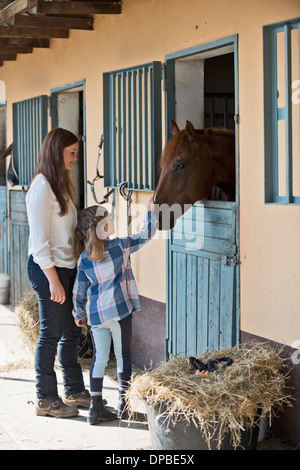 Deutschland, NRW, Korchenbroich, Frau und Mädchen streicheln Pferd im Stall Stockfoto