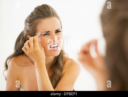 Junge Frau tweezing Augenbrauen unzufrieden Stockfoto