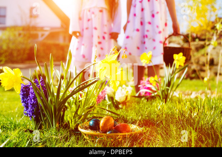 Kinder auf eine Ostereiersuche auf einer Wiese im Frühjahr, im Vordergrund ist ein Korb mit Eiern Stockfoto