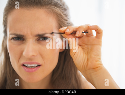 Junge Frau tweezing Augenbrauen unzufrieden Stockfoto