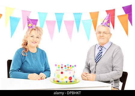 Älteres Paar sitzt am Tisch mit großen Kuchen und feiert Geburtstag Stockfoto