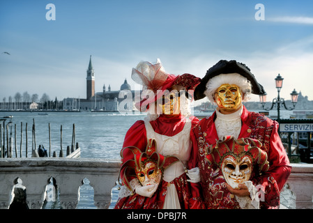 Zwei Teilnehmer tragen rote Kostüme und goldenen Masken im venezianischen Karneval in Venedig, Italien. Stockfoto