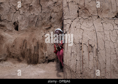 Massai Frau sitzt am Eingang zu einem traditionellen Hütten aus Zweigen mit frischen Kuh eingefügt - Kot und Schlamm, backt Hart unter der heißen Sonne in der Ngorongoro Conservation Area im Krater im Hochland von Tansania Ostafrika Stockfoto