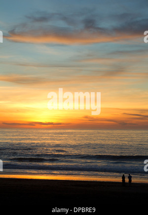 Zwei Personen, die klein im Rahmen den Sonnenuntergang über dem Pazifik beobachten Stockfoto