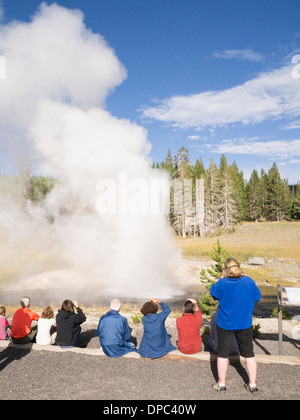 Touristen, die gerade des Ausbruchs des Riverside-Geysir im Yellowstone-Nationalpark, Wyoming, USA Stockfoto