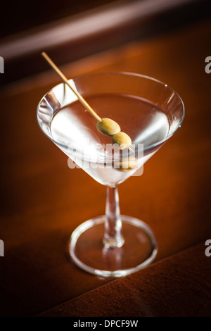 Ein Glas des berühmten klassischen Cocktail Dry Martini mit Olive, vor Ort in Bar aus Holz gedreht. Stockfoto