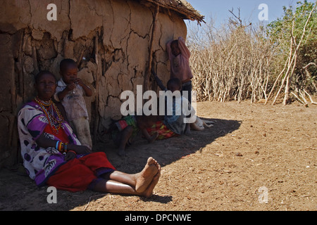 Masai Frau und Kinder sitzen im Schatten einer Hütte Stockfoto