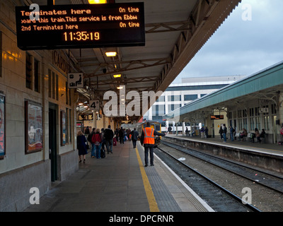 Elektronische Anzeige und Wache auf Plattform mit Zug nähert sich Passagiere warten am Cardiff Central Railway station Wales UK KATHY DEWITT Stockfoto