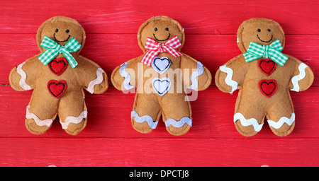 Drei Filz Lebkuchenmänner in einer Reihe auf rot lackierte Board, shabby chic Dekorationen für Weihnachten oder Kinder, süß und lustig Stockfoto