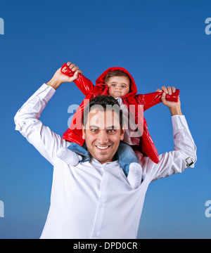 Porträt der fröhlichen jungen Vater mit niedlichen kleinen Sohn sitzen auf seinen Schultern auf blauem Hintergrund klar schüchtern, Spaß im freien Stockfoto