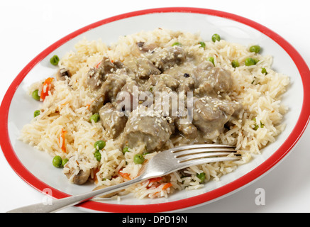 Cremige Lamm Korma Curry garniert mit gerösteten Sesamsamen und serviert auf einem Bett aus Gemüse Reis mit einer Gabel einstechen. Stockfoto