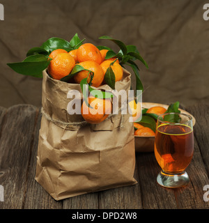 Frische Mandarinen in recyceln Papiertüte und Glas Saft auf Holztisch. Closeup. Stockfoto