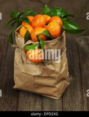 Frische Mandarinen mit Blättern in recyceln Papiertüte auf Holztisch. Stockfoto