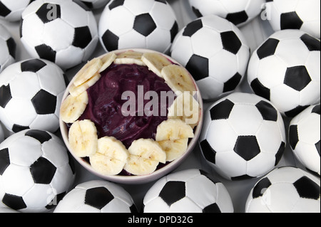 Brasilianischer Kultur auf dem Tisch verfügt über eine Schüssel mit frischen Acai mit Banane, umgeben von Fußball Fußbälle Stockfoto