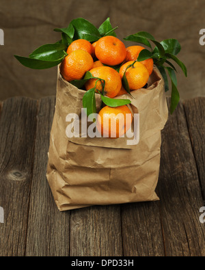 Frische Mandarinen mit Blättern in recyceln Papiertüte auf Holztisch. Closeup. Stockfoto