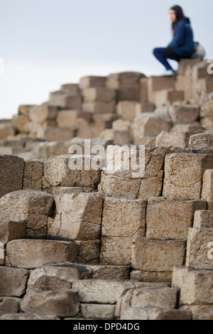 Eine Frau sitzt auf Stapel von Basaltsäulen, die sich die Welt berühmten Giants Causeway in der Grafschaft Antrim. Stockfoto