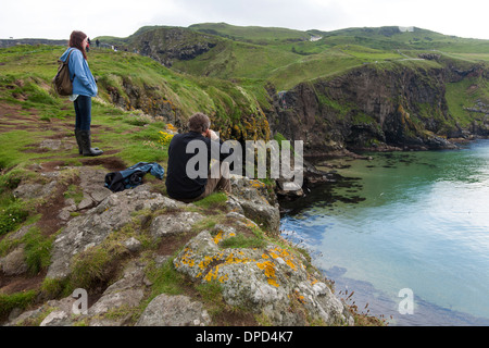 Eine Mädchen schaut auf die Aussicht entlang der Küste von Antrim gesehen von Carrickarede Insel eine Denkmalschutz-Immobilie in Nordirland. Stockfoto