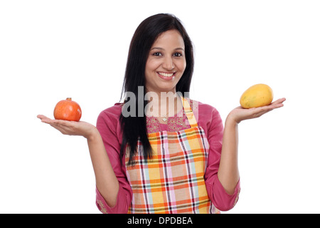 Junge Frau trägt Küchenschürze und hält Obst Stockfoto