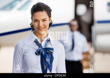 Hübsche Stewardessen lächelnd mit Pilot und Privatjet In Backgr Stockfoto