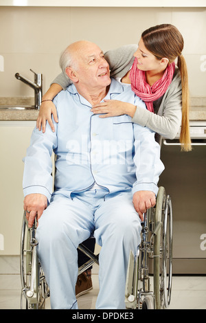 Glückliche junge Frau umarmt einen älteren Mann im Rollstuhl Stockfoto