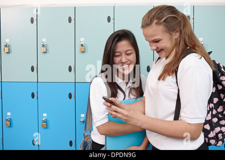 Zwei Teenager Schulmädchen Blick auf Handy neben Schließfächer Stockfoto