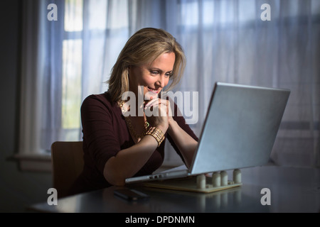 Reife Frau mit Laptop Zuhause sitzen Stockfoto