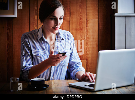 Junge Frau sitzt im Café halten Smartphone, Laptop-Computer mit Stockfoto