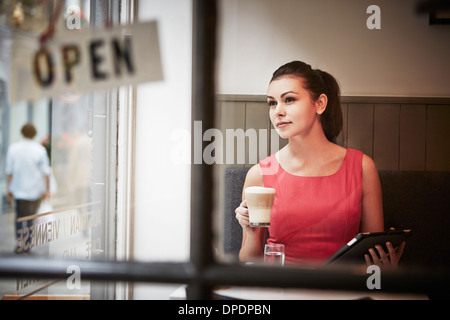 Junge Frau sitzt im Café mit digital-Tablette und Heißgetränk Stockfoto