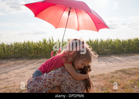 Mutter und Tochter umarmt unter roten Regenschirm Stockfoto