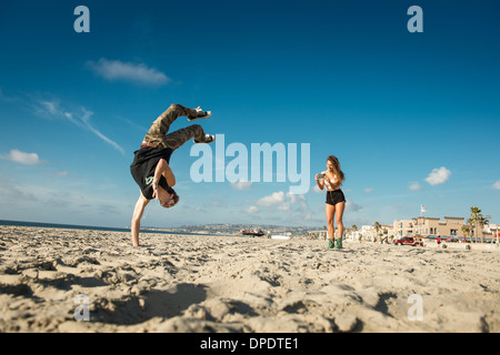 Junge Frau fotografieren Freund tun Backflip am Strand von San Diego Stockfoto