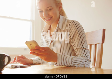 Junge Frau sitzt am Tisch, Blick auf smartphone Stockfoto