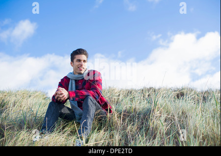 Junger Mann sitzt auf dem Rasen Stockfoto