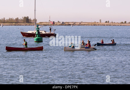 Teenager Rudern am Lake Ontario in Kanus tragen ihre Rettungswesten mit Segelboot hinter ihnen. Stockfoto