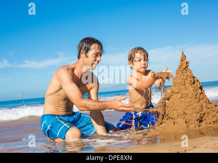 Vater und Sohn spielen zusammen im Sand am tropischen Strand, Gebäude Sand castle Stockfoto
