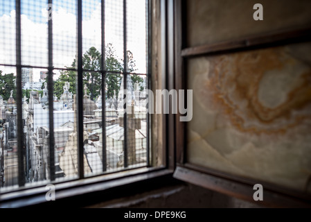 BUENOS AIRES, Argentinien – Ein Blick durch eines der ursprünglichen Fenster aus der Kolonialzeit auf die Basílica de Nuestra Señora del Pilar offenbart den historischen Friedhof Recoleta dahinter. Der 1822 errichtete Friedhof befindet sich neben der Kirche von 1732 und zählt zu den bedeutendsten historischen Stätten von Buenos Aires. Die architektonische Beziehung zwischen diesen beiden historischen Wahrzeichen veranschaulicht die historische Bedeutung des Stadtteils Recoleta. Stockfoto